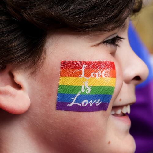 Young person with rainbow sticker on their cheek that reads love is love