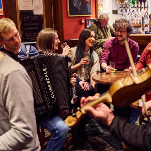 A group of friends in a pub with musicians playing the violin and accordion